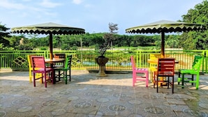 An outdoor patio with tiled flooring, green and red chairs, and two green umbrellas. - Graha Wisata (Kotabumi)