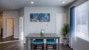 A dining area with a gray table, two blue cushioned chairs, a glass vase with lemons, and a blue abstract painting on the wall. - Cozy 2-Bedroom Condo in Vibrant Urban Omaha with Convenient Designated Parking (Omaha)