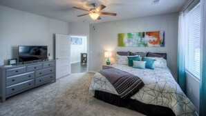 A bedroom with a bed, a dresser, a television, a ceiling fan, and a painting on the wall. - Cozy 2-Bedroom Condo in Vibrant Urban Omaha with Convenient Designated Parking (Omaha)
