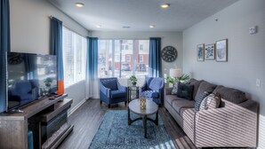 A modern living room with a flat-screen TV, blue armchairs, a sofa, and a coffee table. - Cozy 2-Bedroom Condo in Vibrant Urban Omaha with Convenient Designated Parking (Omaha)