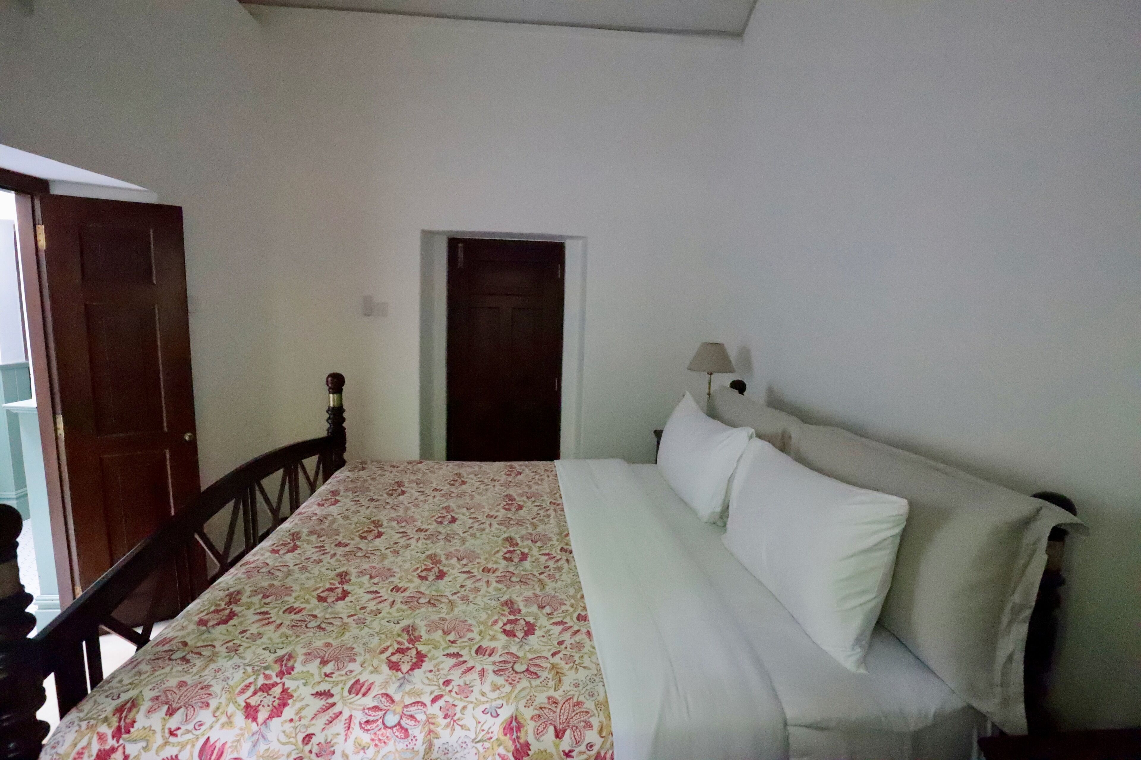 Quarto com cama, cadeira de madeira, porta e abajur.