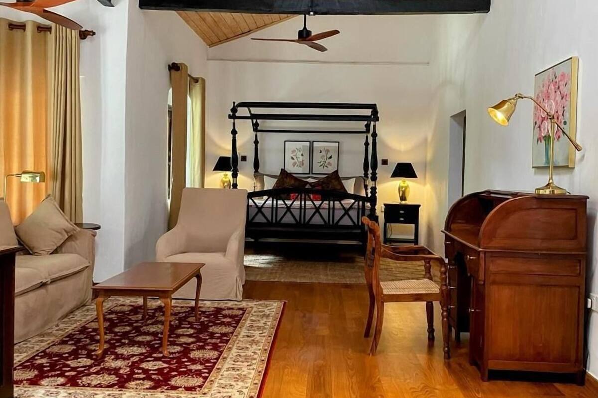 A spacious room with a wooden ceiling, a bed with a metal frame, a wooden desk, a chair, and a sofa.