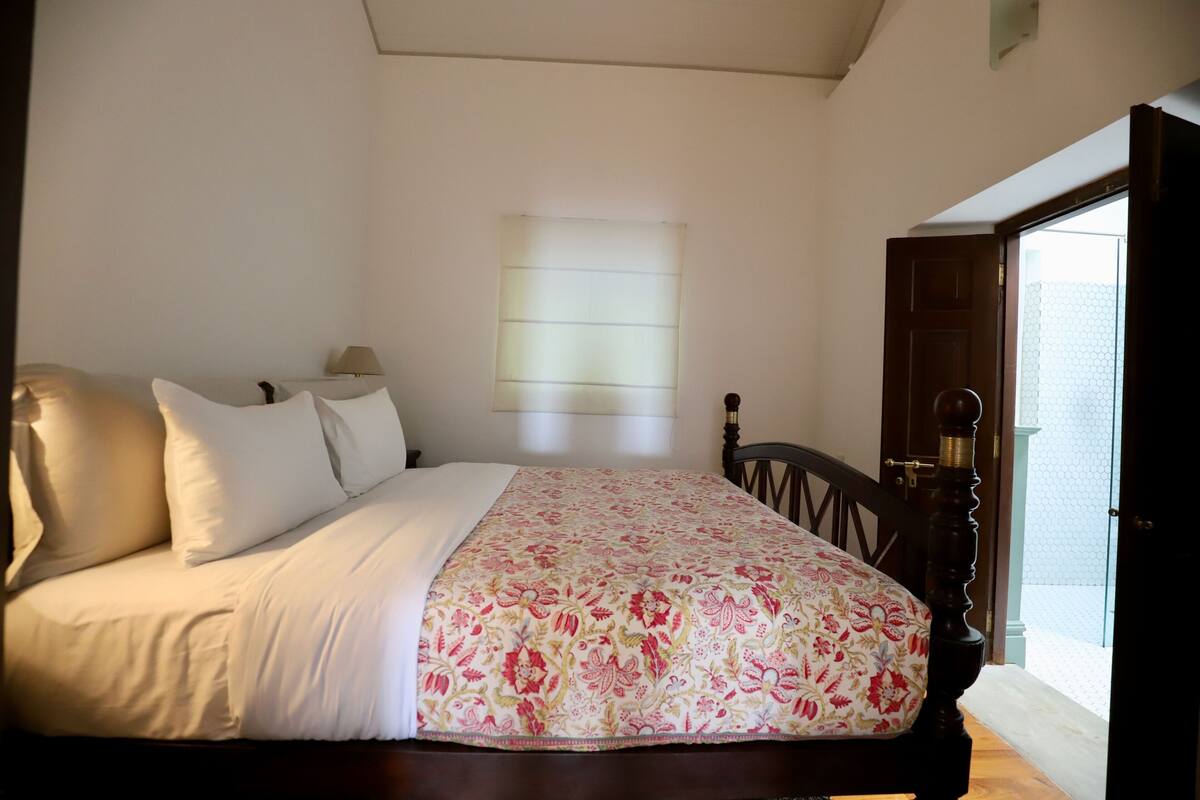 A bedroom with a bed, pillows, a lamp, and a window with blinds.