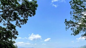 Une pelouse bien entretenue, agrémentée de fleurs rouges au premier plan, entourée d’arbres et offrant une vue dégagée sur les montagnes lointaines sous un ciel bleu.