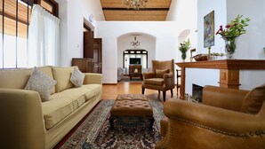 Un salon spacieux avec un canapé beige, un fauteuil en cuir marron, un tapis à motifs et un plafond en bois.
