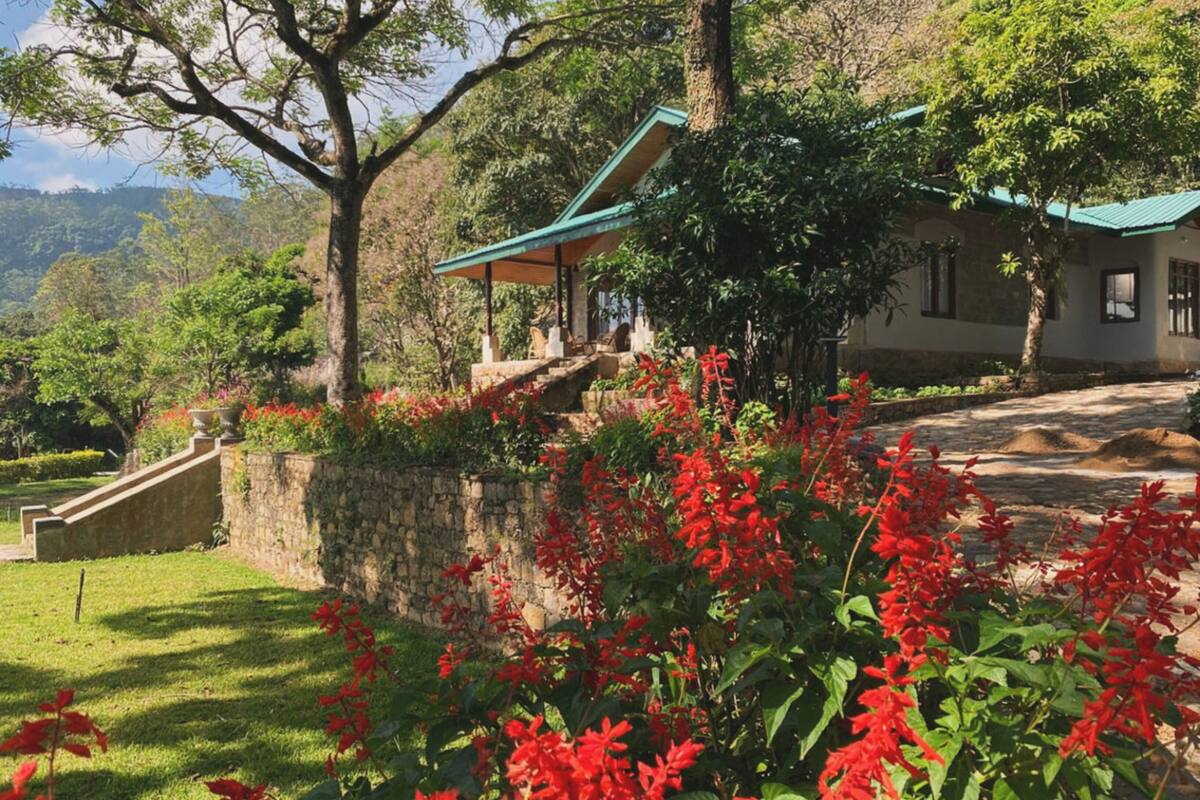 A traditional building with a green roof, surrounded by lush greenery and red flowers.