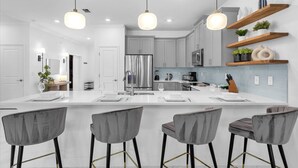 A modern kitchen with a large island, bar stools, pendant lights, and built-in appliances. - Upstay24-PPLHomeThemeRoomsPoolSpaCinema (Kissimmee)