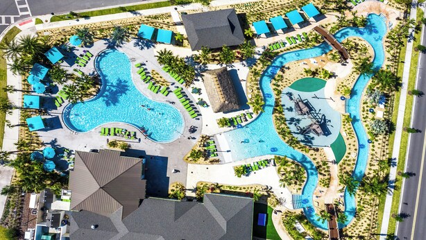 An aerial view of a resort with a large swimming pool, multiple lounge areas, and a water slide. - Upstay24-PPLHomeThemeRoomsPoolSpaCinema (Kissimmee)