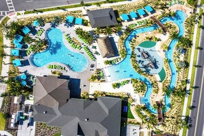 An aerial view of a resort with a large swimming pool, multiple lounge areas, and a water slide. - Upstay24-PPLHomeThemeRoomsPoolSpaCinema (Kissimmee)