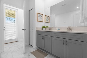 A modern bathroom with grey cabinets, a large mirror, and a window with blinds. - Upstay24-PPLHomeThemeRoomsPoolSpaCinema (Kissimmee)