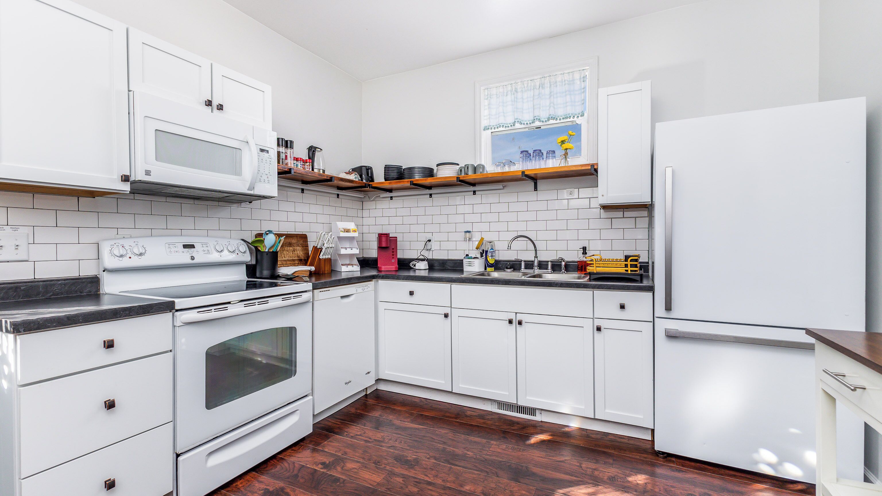 A modern kitchen with white cabinets, a stainless steel refrigerator, a microwave, and a stove.