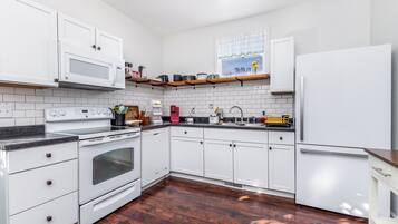 A modern kitchen with white cabinets, a stainless steel refrigerator, a microwave, and a stove.