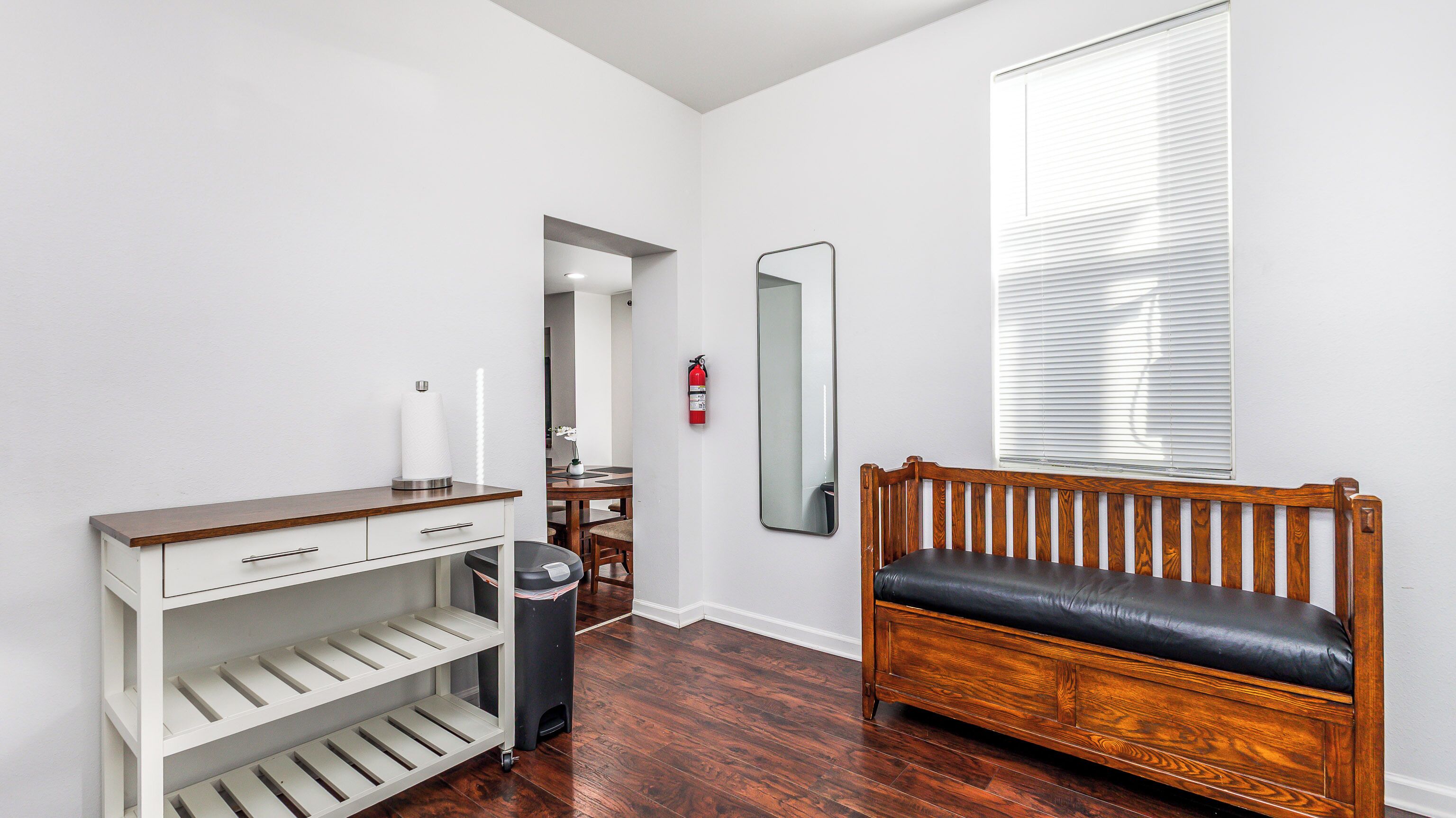 Une pièce avec un banc en bois, un bureau blanc doté d’étagères, un miroir et un extincteur fixé au mur.