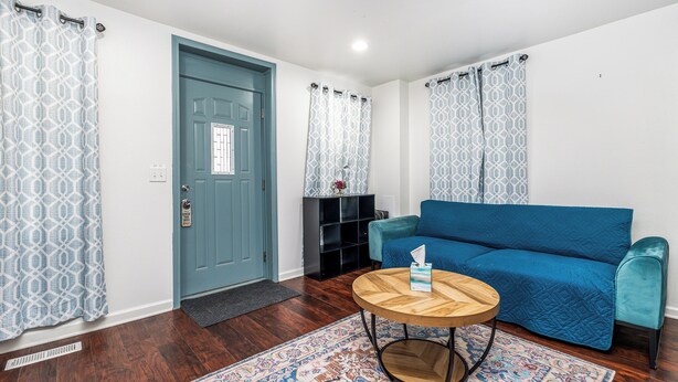 A living room with a blue sofa, a wooden coffee table, and patterned curtains. - Cheerful home by Millwork District/Farmers Market (Dubuque)