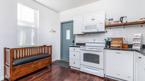 A compact kitchen with white appliances, a wooden bench, and a blue door. - Cheerful home by Millwork District/Farmers Market (Dubuque)