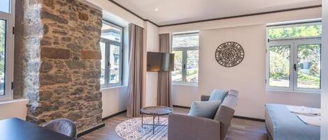 A modern living room with a stone wall, a flat-screen TV, a sofa, a small round table, and a bed.