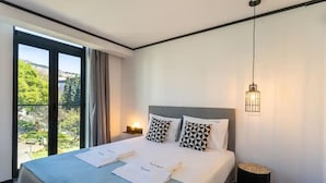 Une chambre d’hôtel moderne avec un grand lit, une vue sur la verdure et un luminaire suspendu.