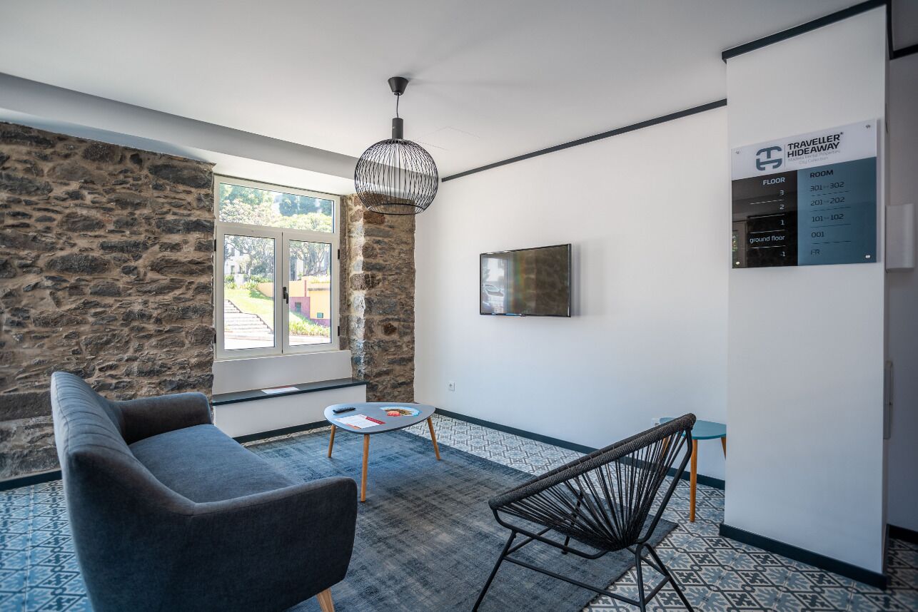 Une pièce moderne avec un mur en pierre, une grande fenêtre, un canapé, un fauteuil, une petite table et un luminaire suspendu.