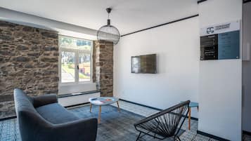 Une pièce moderne avec un mur en pierre, une grande fenêtre, un canapé, un fauteuil, une petite table et un luminaire suspendu.