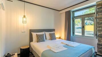 A hotel room with a bed, a bedside table, a lamp, and a window with a view of the outside.