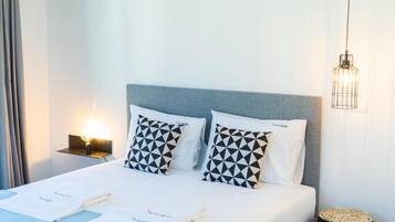 A neatly made bed with geometric patterned pillows, a bedside lamp, and a small round table with a woven base.
