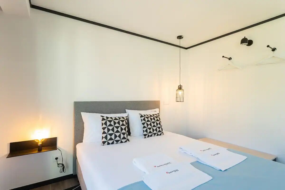 Une chambre d’hôtel avec un lit, deux oreillers, une table de chevet, une lampe et un ventilateur de plafond.