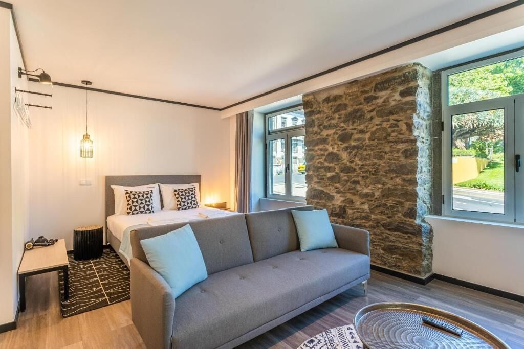 A modern bedroom with a bed, a sofa, a stone accent wall, and large windows.