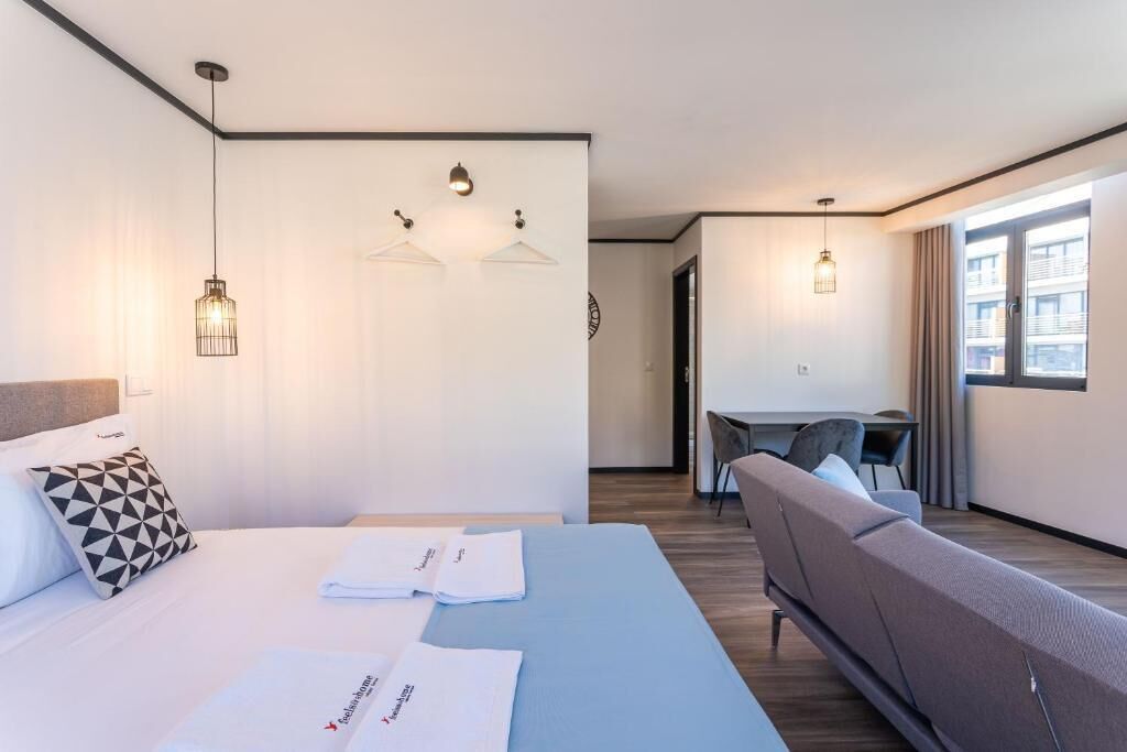 A modern hotel room with a bed, a sofa, a desk, and two pendant lights.