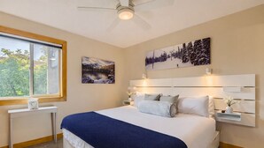 Ein Schlafzimmer mit einem großen Bett, einem Nachttisch, einem an der Wand montierten Regal und einem Deckenventilator.