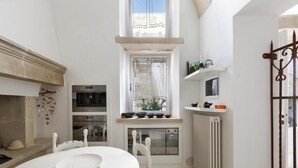 A compact kitchen with a white table, a built-in oven, a microwave, and a window with a curtain. - Garibaldi Luxury, in complete luxury and relaxation (Otranto)