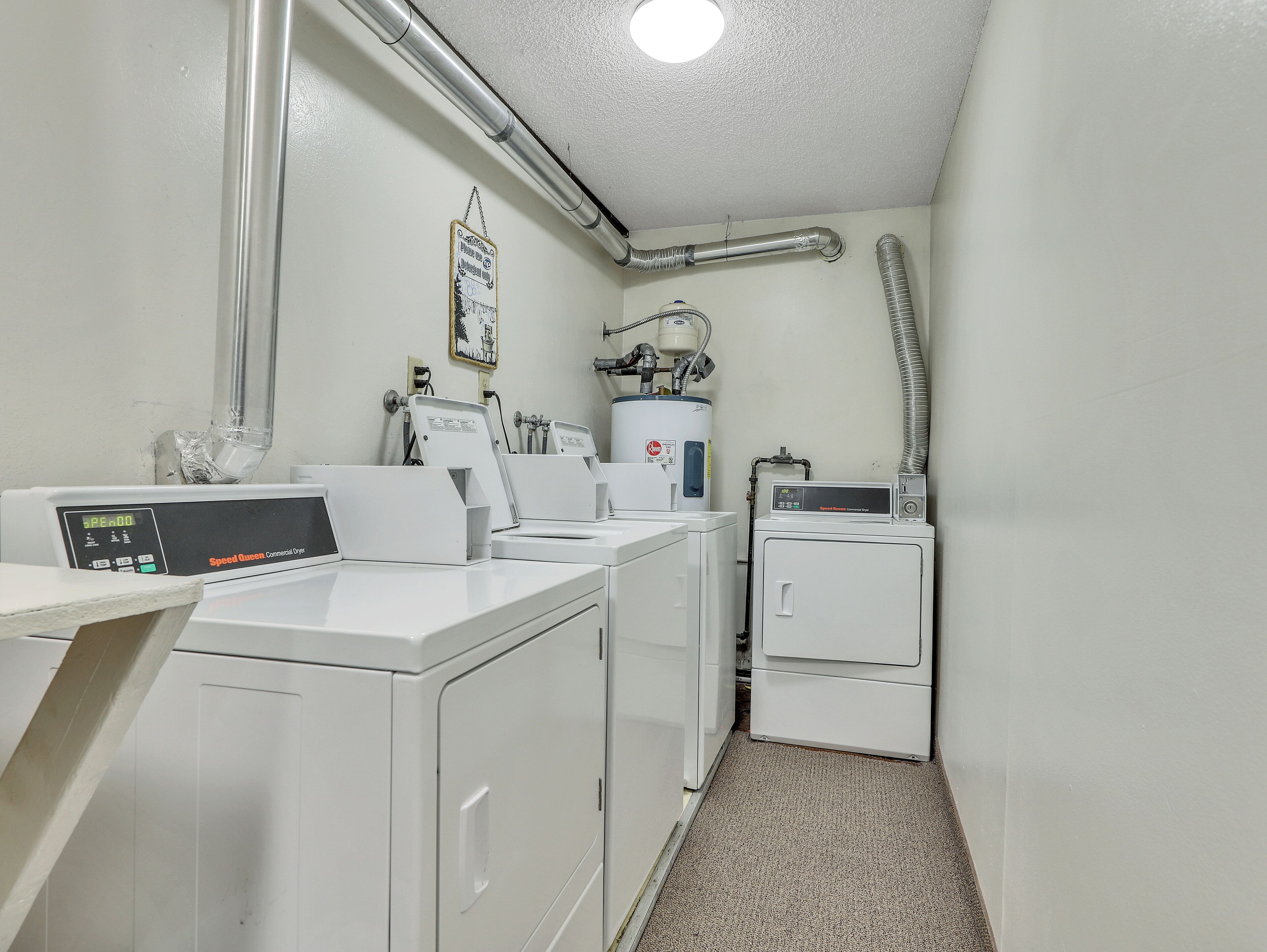 A laundry room with industrial dryers, a water heater, and a ventilation system.