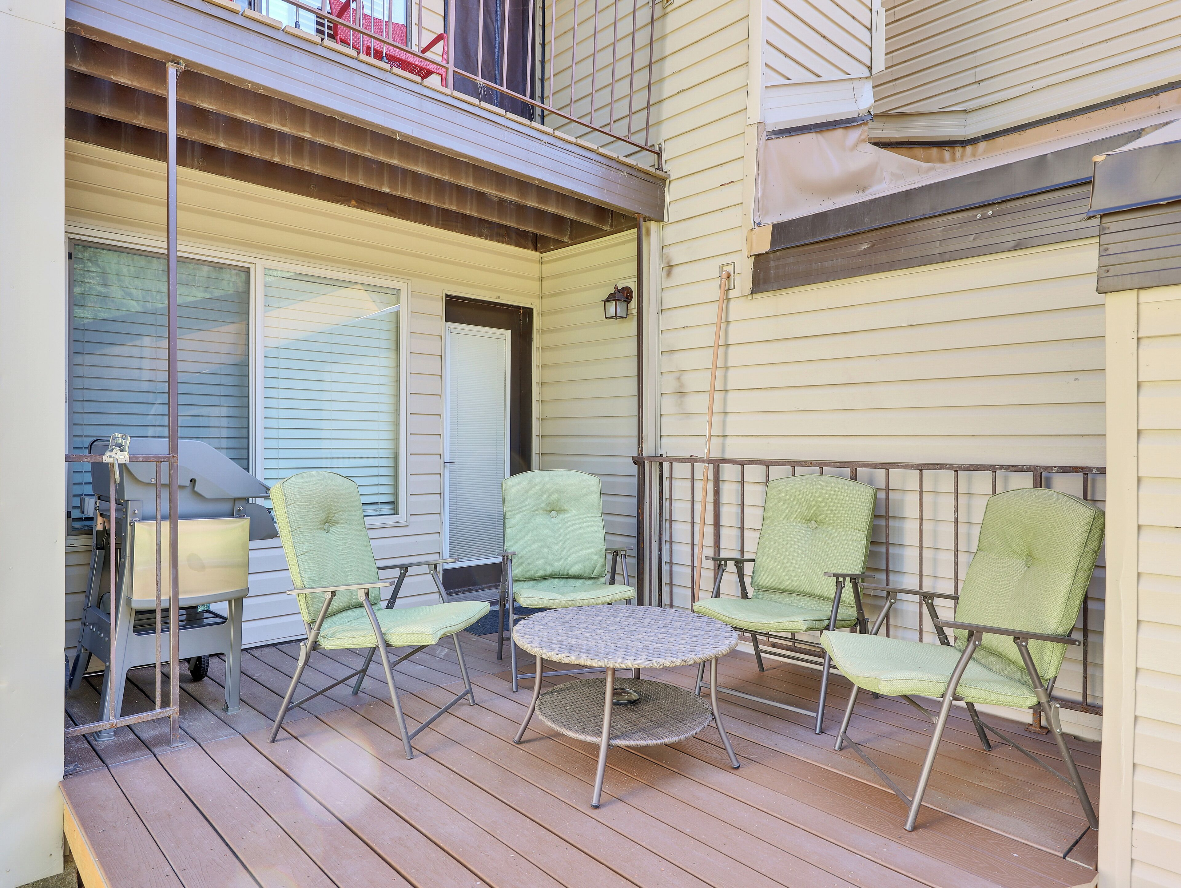 A covered outdoor patio with four green chairs and a round table.