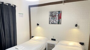 Een hotelkamer met twee enkele bedden, een klein bureau, een spiegel en een kunstwerk aan de muur.