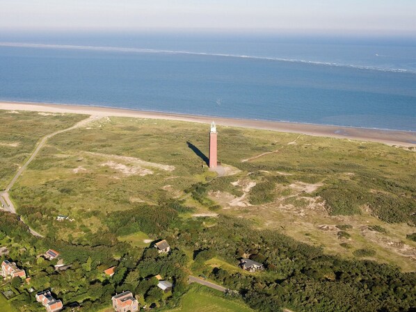 An aerial view of a coastal area with a lighthouse, a beach, and scattered buildings.
