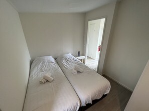 A small, clean room with two beds, a small table, and a door leading to a balcony. - Enticing Chalet Beachside (Hellevoetsluis)