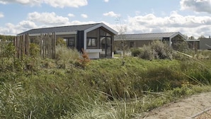 Une maison moderne dotée d’une grande façade en verre, entourée d’une végétation luxuriante.