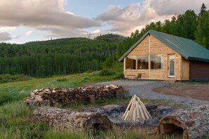 Eine Blockhütte mit Metall-Dach, einem Steinkamin und bewaldeter Umgebung.