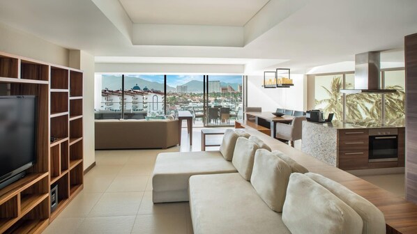 A modern living room with a large TV, a sofa, a dining area, and a kitchen with a view of the city.