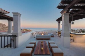 An outdoor seating area with a view of the sea, featuring a wooden table, cushioned seating, and a pergola structure. - Oceanview Luxury Apartment with Pool & Spa Access (Cabo San Lucas)