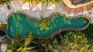 Una piscina grande y de forma peculiar rodeada de abundante vegetación y estructuras blancas.
