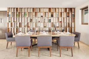A conference room with a long table, six chairs, and a wooden bookshelf with various decorative items.