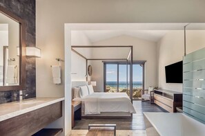 A modern bedroom with a large bed, a bathroom with a large mirror, and a view of the ocean.