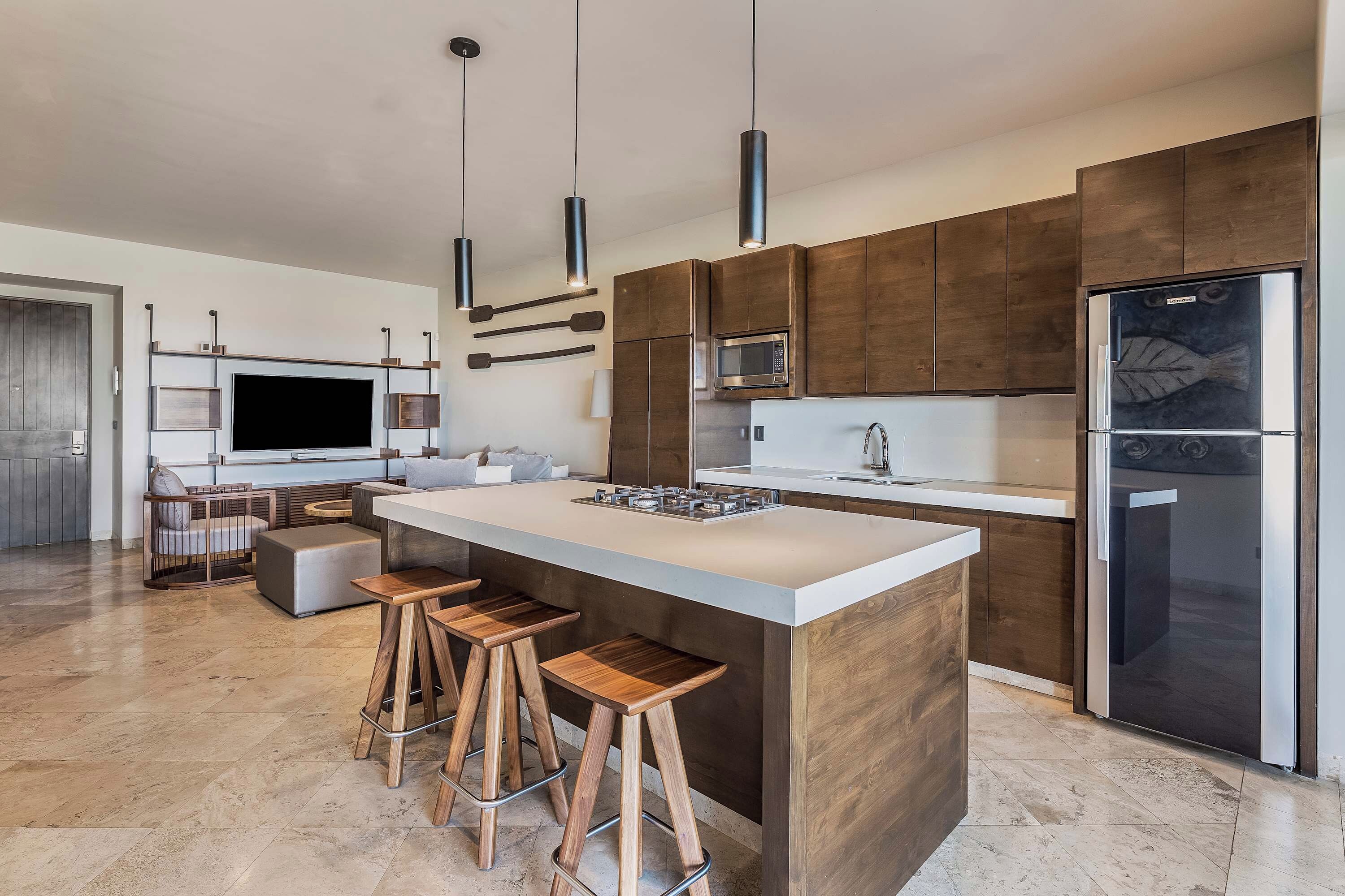 A modern kitchen with a large island, bar stools, a built-in oven, and a refrigerator.
