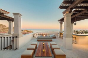 An outdoor seating area with a wooden table, cushioned seating, and a view of the beach.