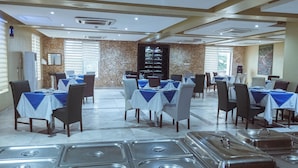 A restaurant with multiple tables set for dining, a buffet area with trays, and a brick wall with a mirror. - Fullmoon Hotels Owerri (Owerri)
