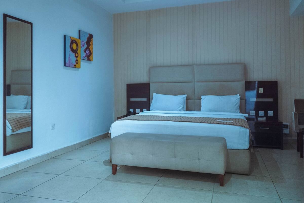 A bedroom with a large bed, a bedside table, a nightstand, a mirror, and artwork on the wall.