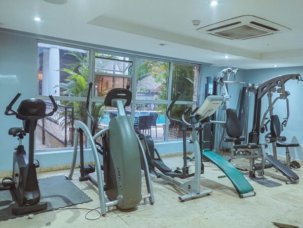 Un gimnasio con diverso equipo de ejercicio, ventanas amplias y vistas al exterior.