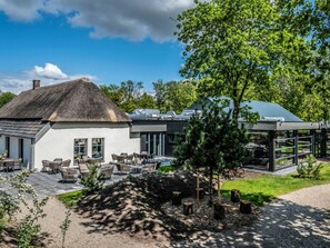 A modern building with a thatched roof structure, outdoor seating area, and a glass-enclosed section. - Villa in Schaijk Near Forest & Water (Schaijk)