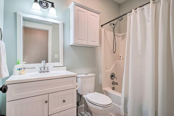 A bathroom with a white vanity, a toilet, a bathtub with a showerhead, and a curtain. - The Southport Cottage! (Southport)