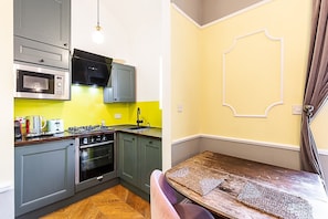 A compact kitchen with a microwave, stove, and sink, and a small dining area with a table and chairs. - Stylish Hyde Park Gem (London)